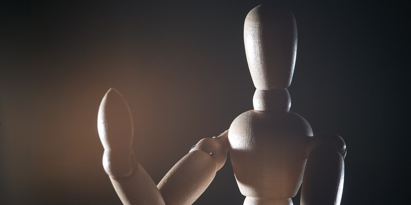 A wooden drawing mannequin posed against a dark background